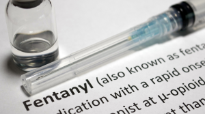 A syringe and a vial rest on a paper displaying the word "Fentanyl" and its partial definition, highlighting concerns about Fentanyl in San Joaquin County.