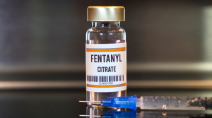 A vial labeled "Fentanyl Citrate" stands upright next to a syringe on a reflective surface, with a blurred background—highlighting the growing concern reflected in recent fentanyl statistics from San Joaquin County.